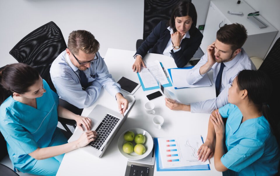 Profisisonais da saúde reunidos em uma mesa discutindo a gestão de planos de saúde.