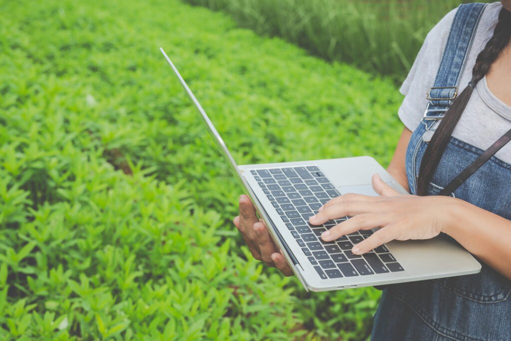 Foto mostra profissional com laptop em meio a uma plantação, mostrando a transformação da tecnologia e necessidade do ERP para agronegócio.